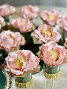 Blush color fabric flowers holding a gold truffle. The flowers sits on top a votive which has gold accent bids