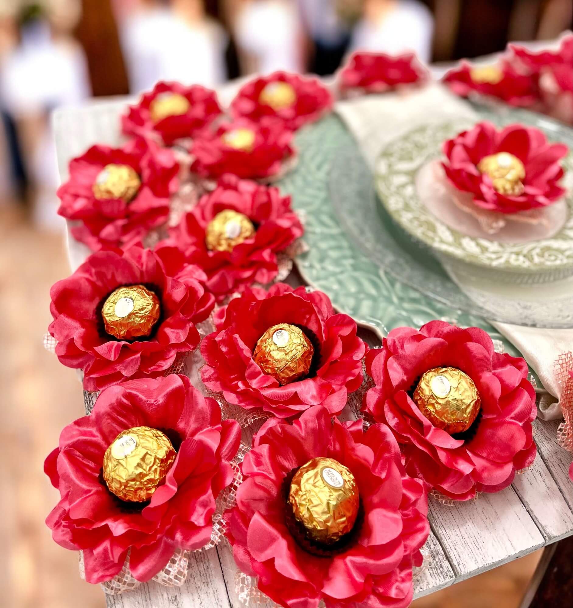 coral flower-shaped containers with gold chocolates on a wooden surface.