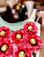 coral flower-shaped containers with gold chocolates on a wooden surface.
