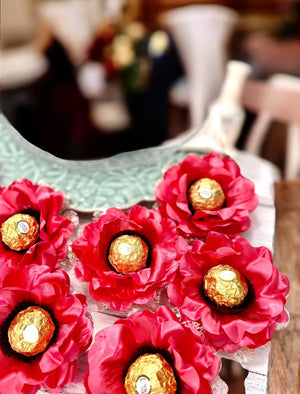 coral flower-shaped containers with gold chocolates on a wooden surface.
