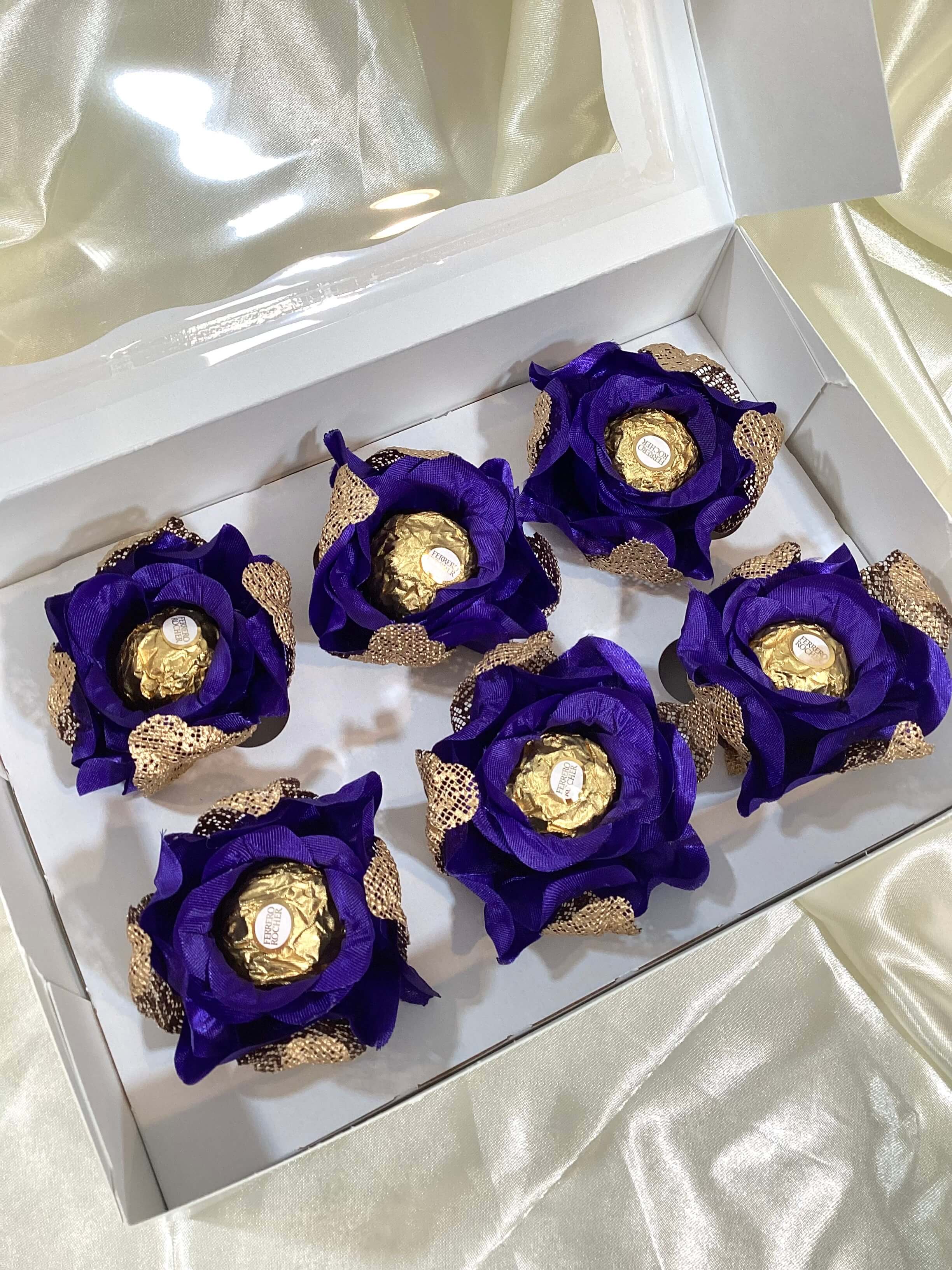 Decorative royal blue roses flowers with gold mesh holding a chocolate in a box of 6 roses.