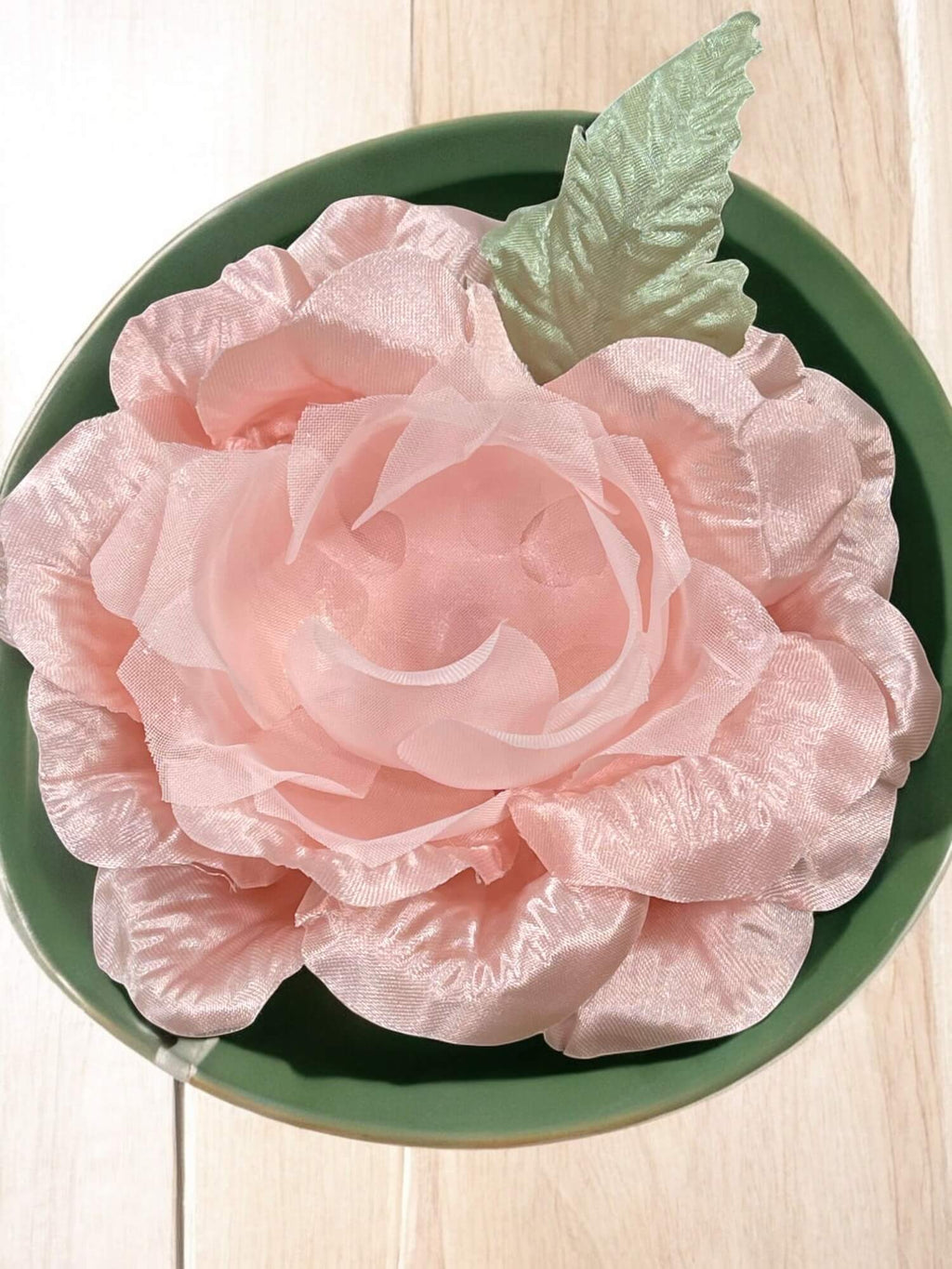 Pink flower on a green plate with a light wooden background