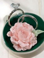 Pink rose on a green dish with two silver rings on a white background