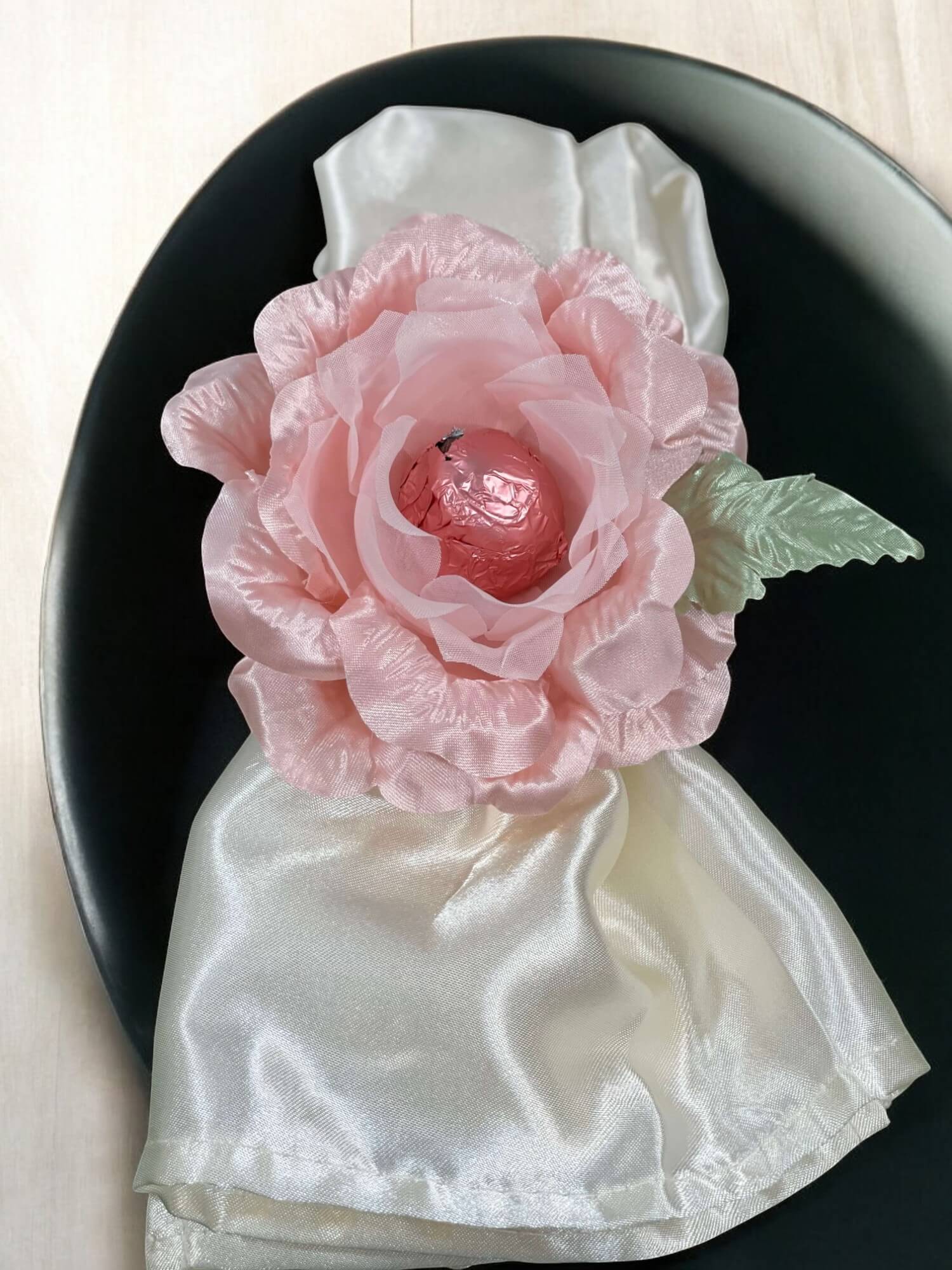 Pink flower on a white napkin with a black plate underneath