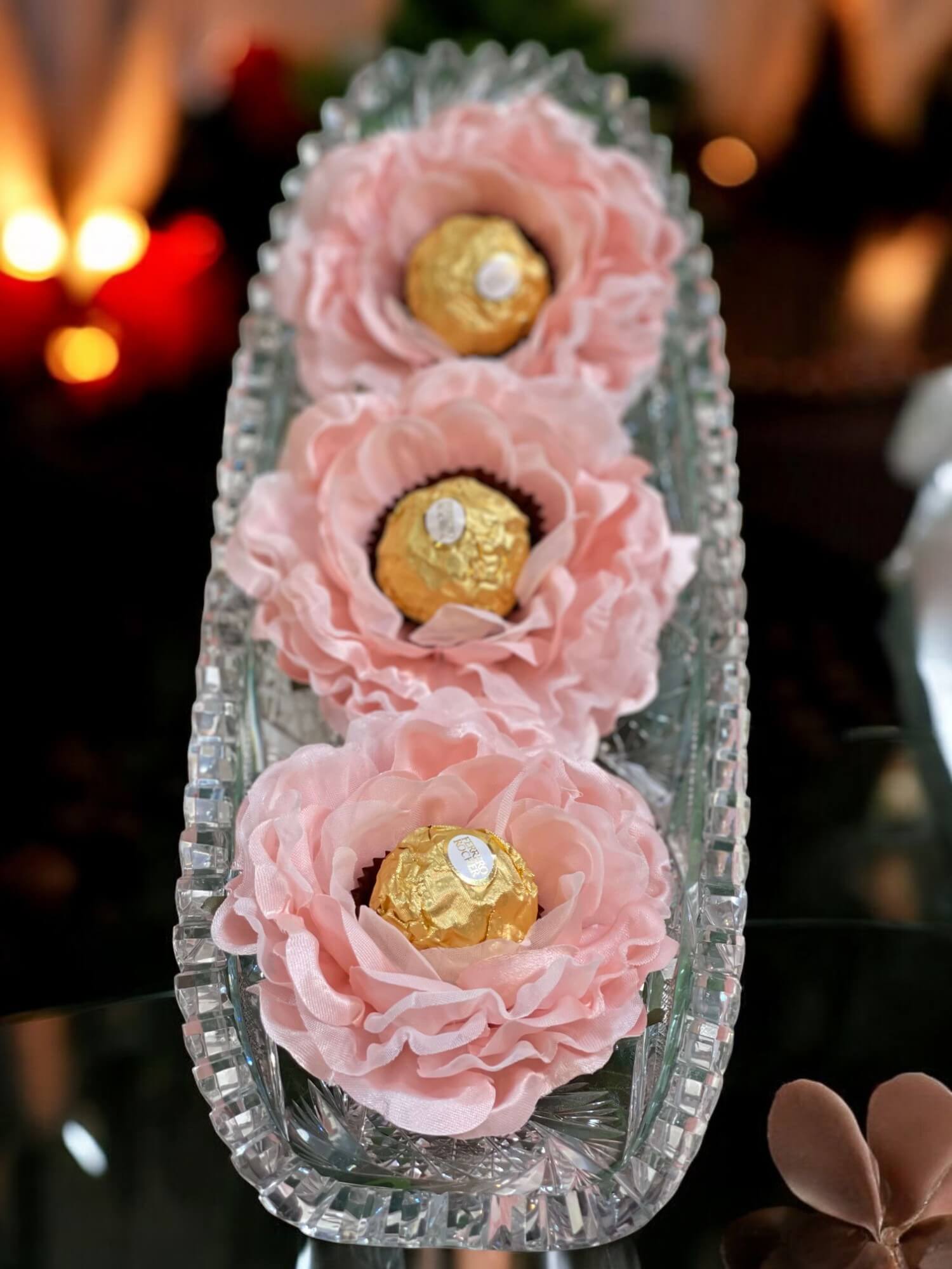 Decorative tray with pink flower-shaped containers holding gold Ferrero Rocher chocolates.