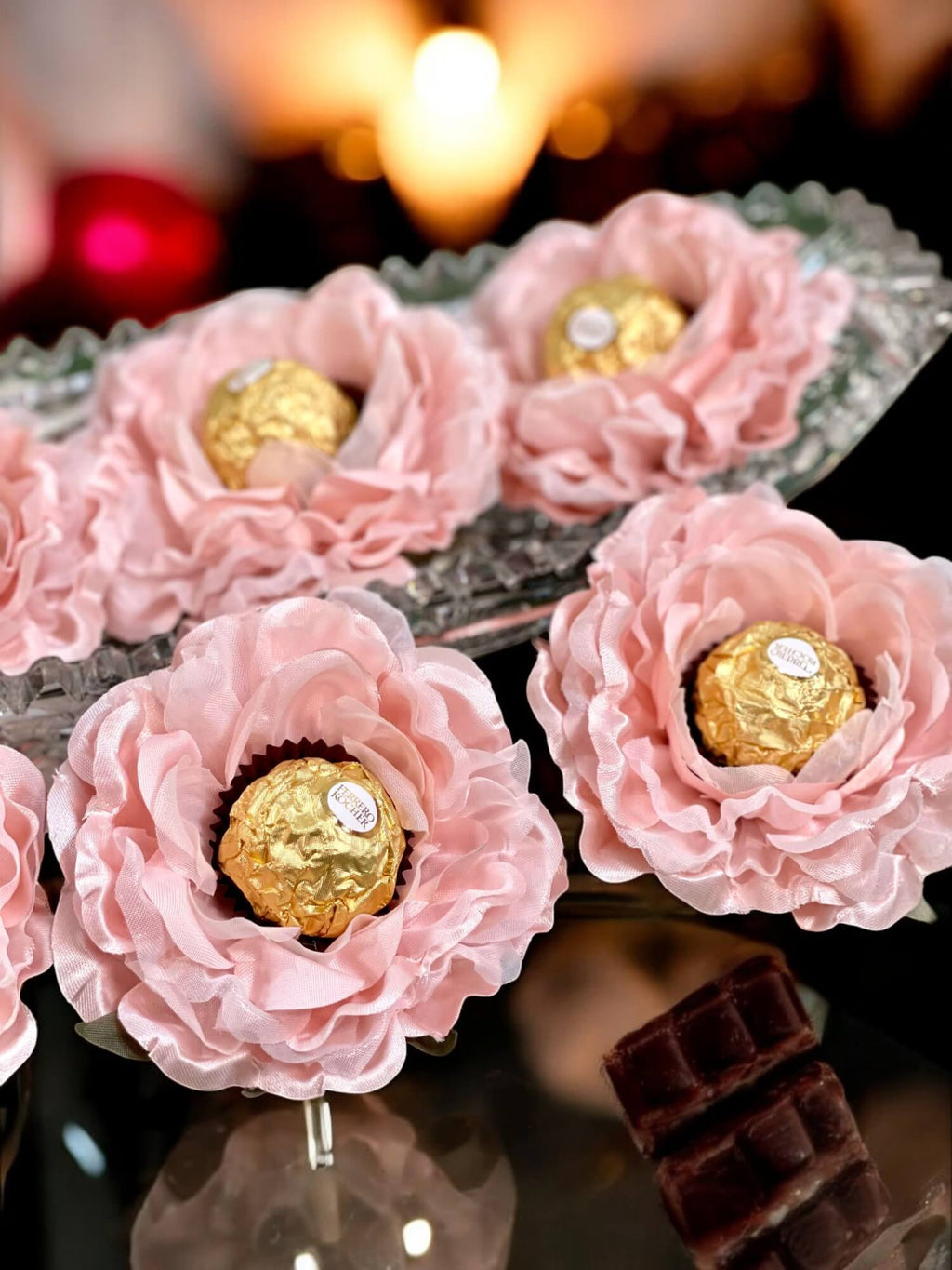 Decorative pink fabric flower holding round chocolate  on a reflective surface.