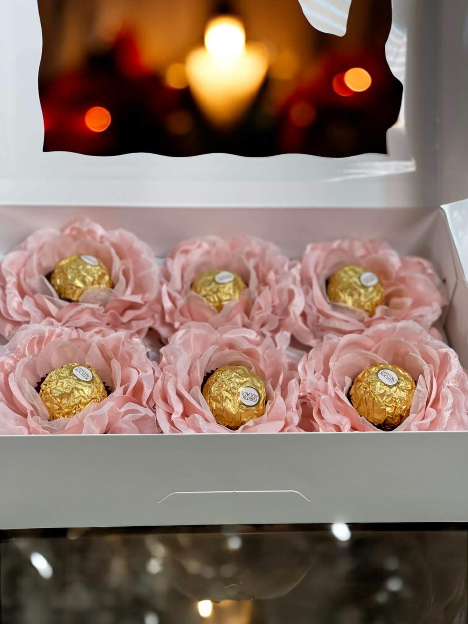 Box of chocolates wrapped in pink flower petals with a blurred candlelit background