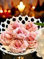 Decorative blush flowers holding pink macaron cookies on a white plate with a blurred candlelit background