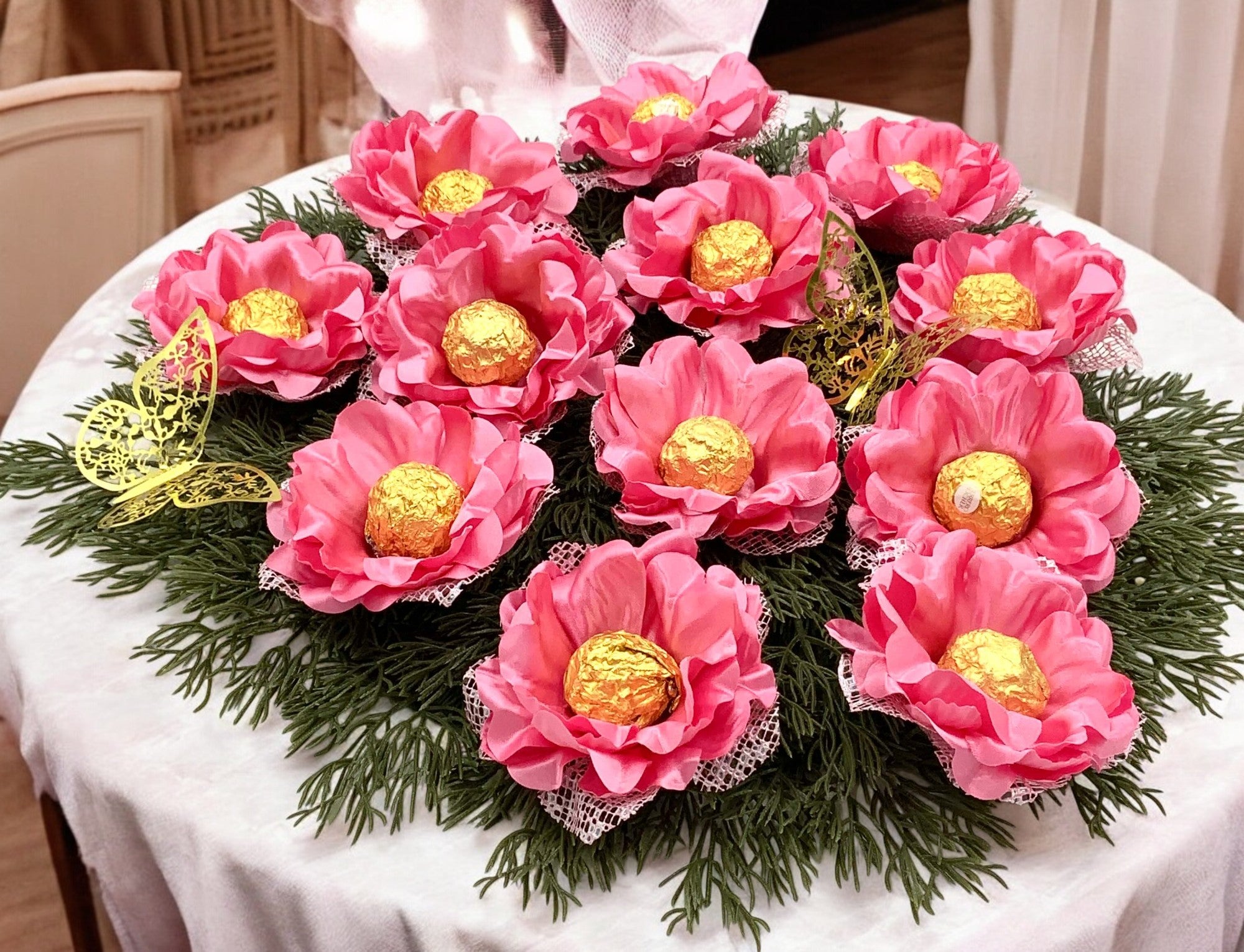 Decorative arrangement of pink flowers with gold centers on a white tablecloth.