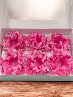 Pink fabric flowers  in a white box on a wooden surface. Flowers have an open in a round shape to hold candies or chocolates.