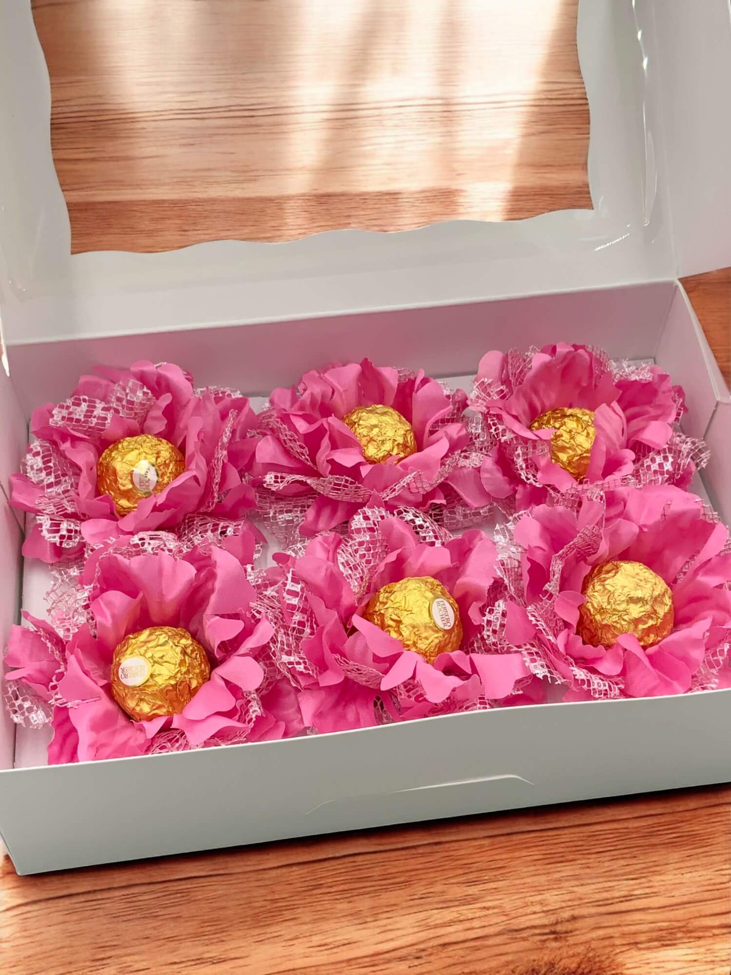 Ferrero Rocher chocolates arranged in a decorative manner with pink flowers in a white box.