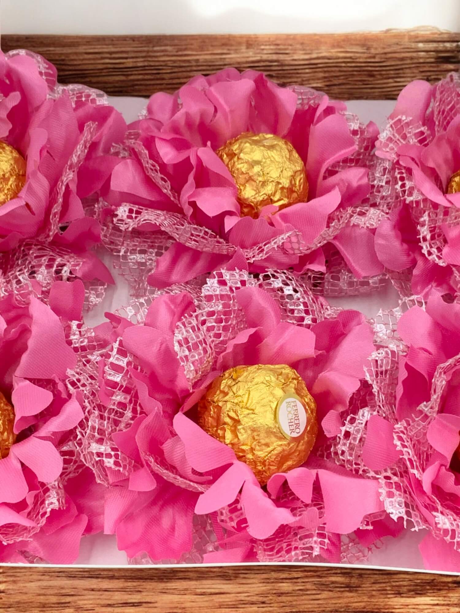 Pink flower-shaped packages with gold chocolates inside on a wooden surface.