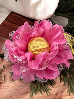 Pink flower arrangement with a gold chocolate truffle in the center on a wooden surface.