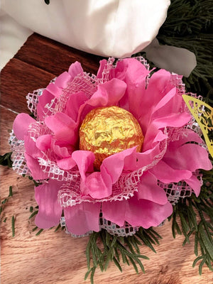 Pink flower arrangement with a gold chocolate truffle in the center on a wooden surface.