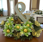 Decorative centerpiece with green fabric flowers chocolate holders, greenery, gold chocolate balls inside each flower, and a large ampersand on a table.