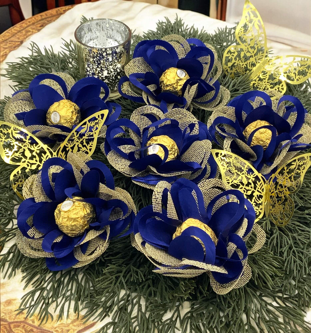 Centerpieces with royal blue and gold flowers sitting on greenery.