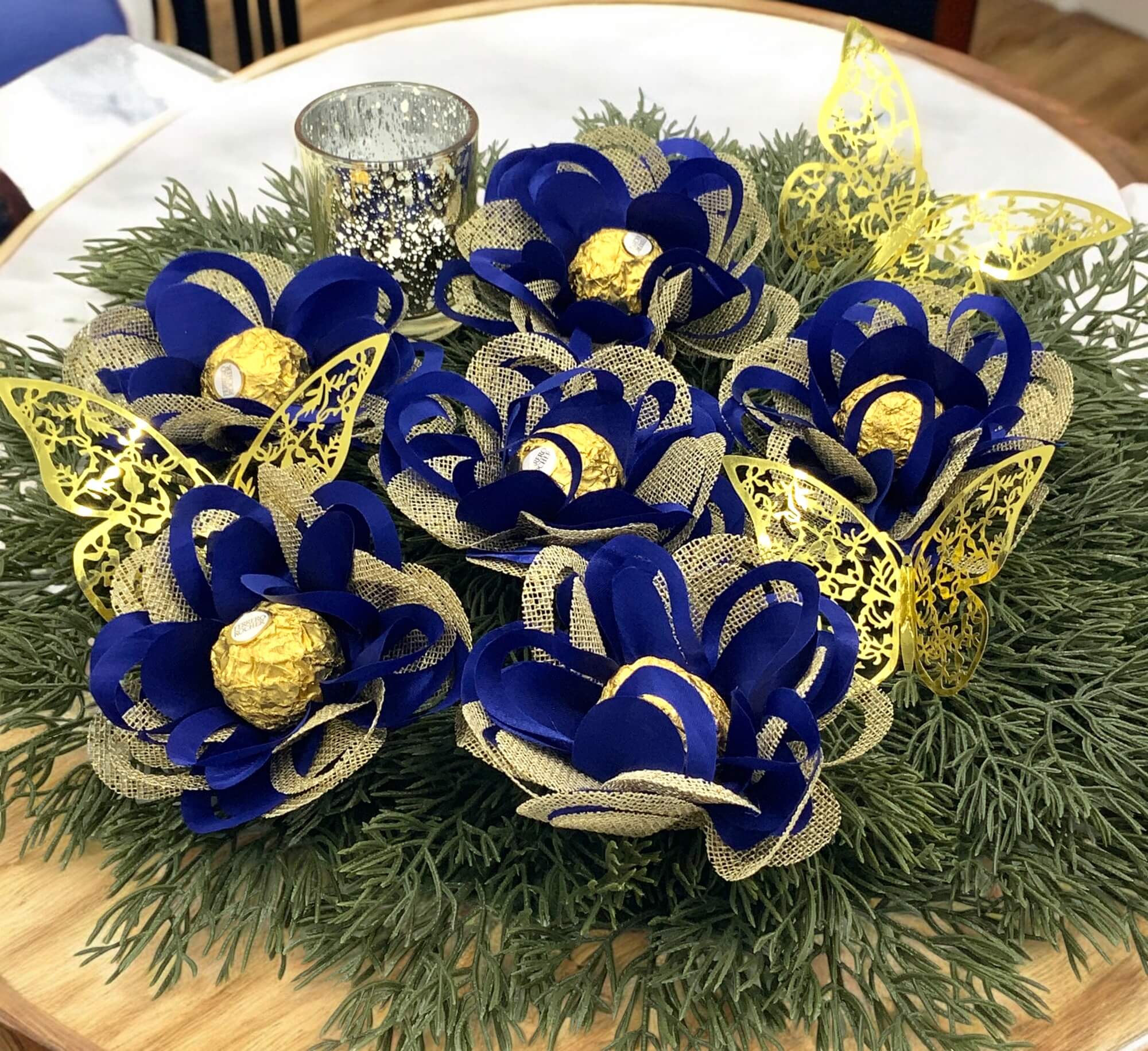 Centerpieces with royal blue and gold flowers sitting on greenery.