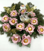 Decorative centerpiece with pink flowers, gold chocolate, and silver rings on a white background