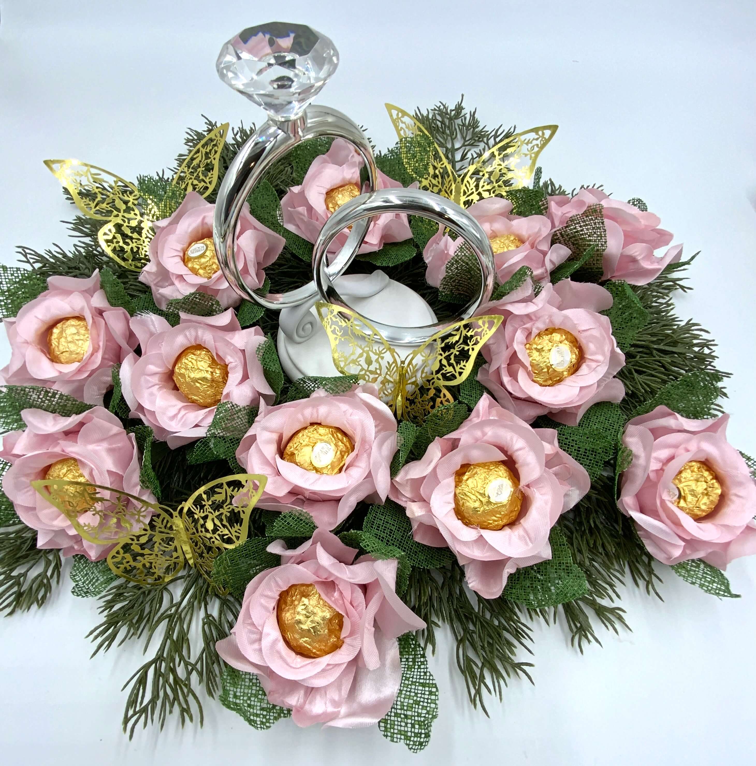 Decorative centerpiece with pink flowers, gold chocolate, and silver rings on a white background