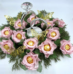 Decorative centerpiece with pink flowers, gold chocolate, and silver rings on a white background