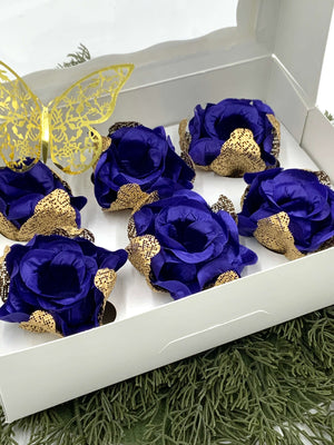 Blue roses with gold accents in a white box on a green surface