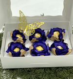Decorative royal blue and gold flowers in a white box with a butterfly design on a green textured background.
