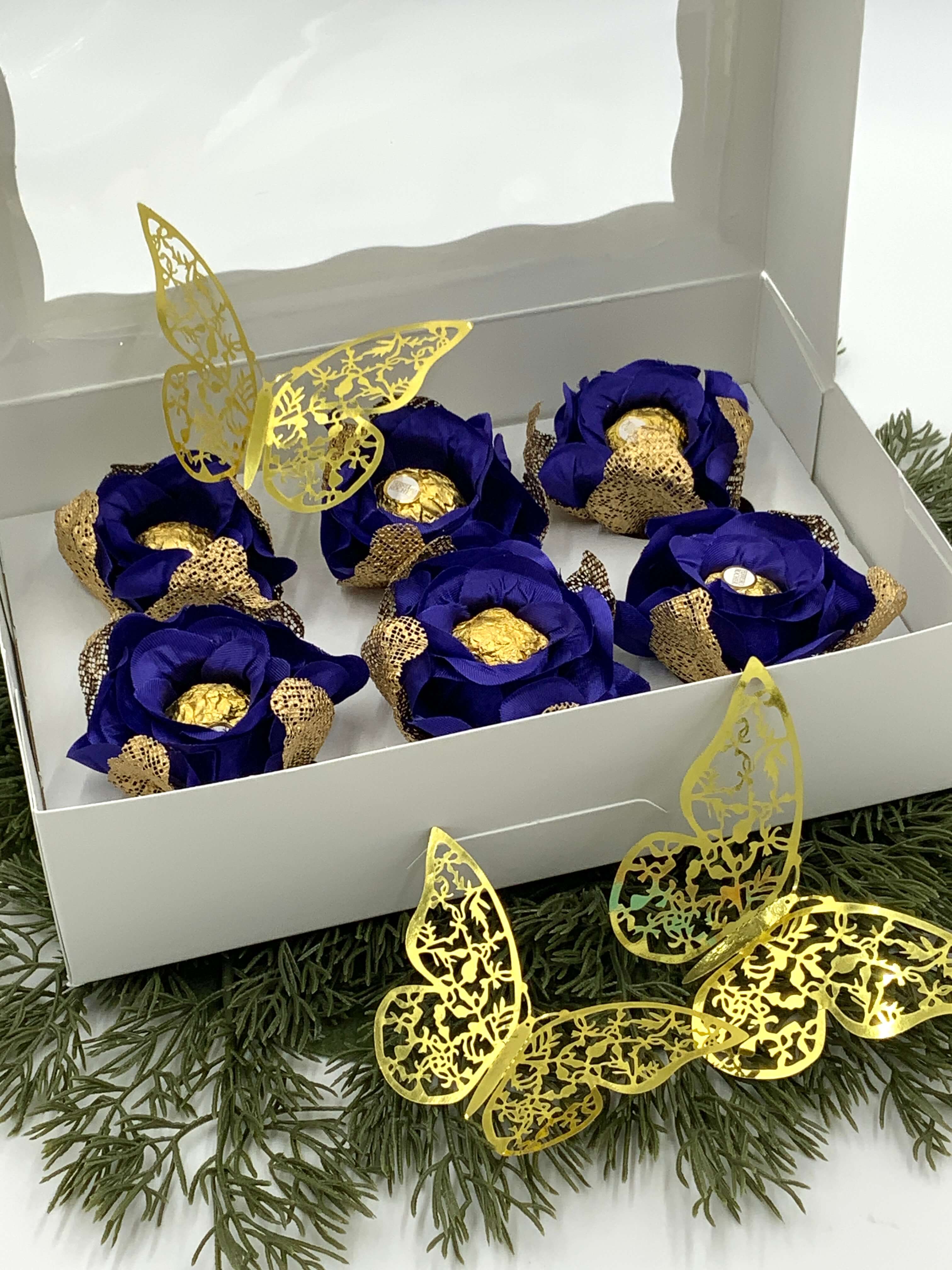 Decorative items with blue flowers and gold accents in a white box, surrounded by greenery.