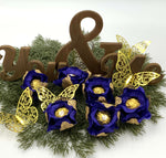 Decorative arrangement with blue flowers, gold accents, and wooden letters on a white background