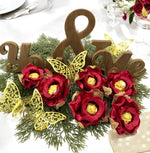 Decorative table setting with red flowers, gold butterflies, and wooden letters spelling 'You & Me' on a white tablecloth.