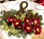 Decorative table setting with wooden letters, red flowers, and gold butterflies on a white plate.