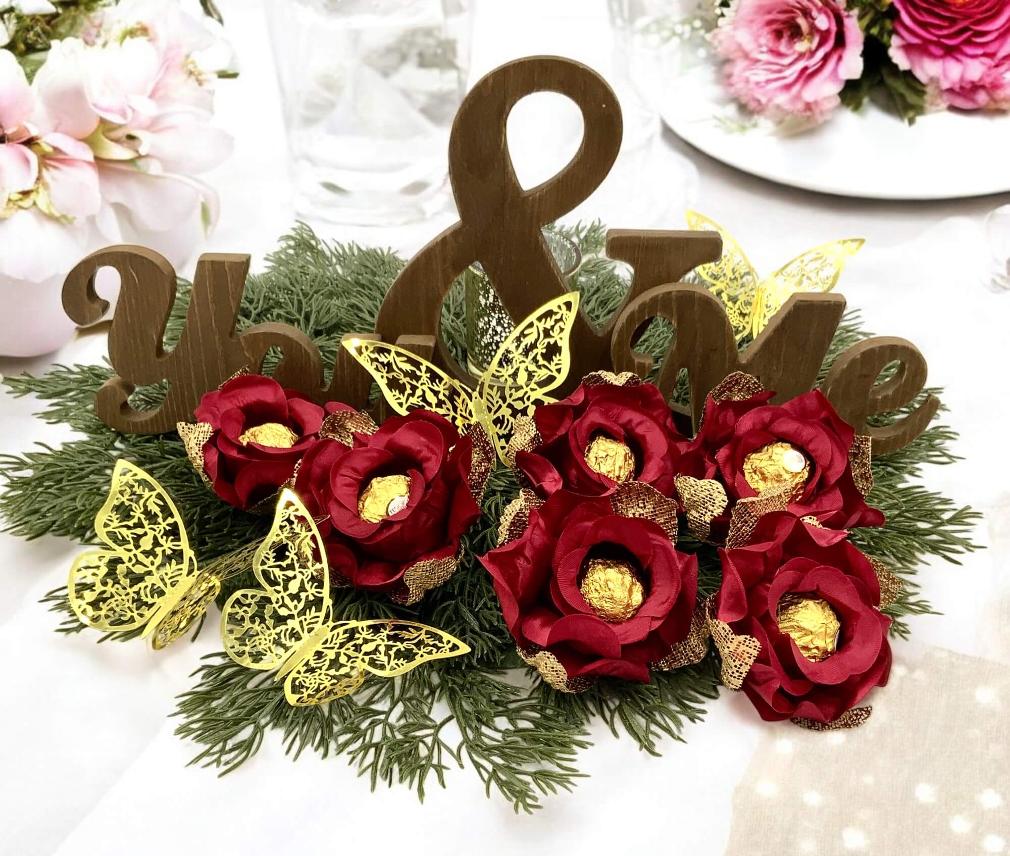 Decorative arrangement with red flowers, gold butterflies, and wooden letters on a white background