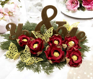 Decorative arrangement with red flowers, gold butterflies, and wooden letters on a white background