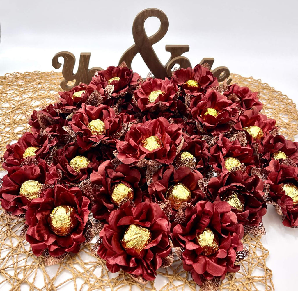 Decorative arrangement of maroon flowers with gold chocolates on a white background