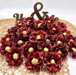 Decorative arrangement of maroon flowers with gold chocolates on a white background
