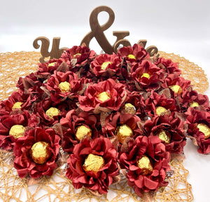 Decorative arrangement of maroon flowers with gold chocolates on a white background