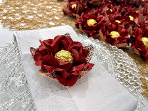 Decorative arrangement of maroon flowers with gold chocolates on a white background