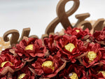 Decorative arrangement of maroon flowers with gold chocolates on a white background