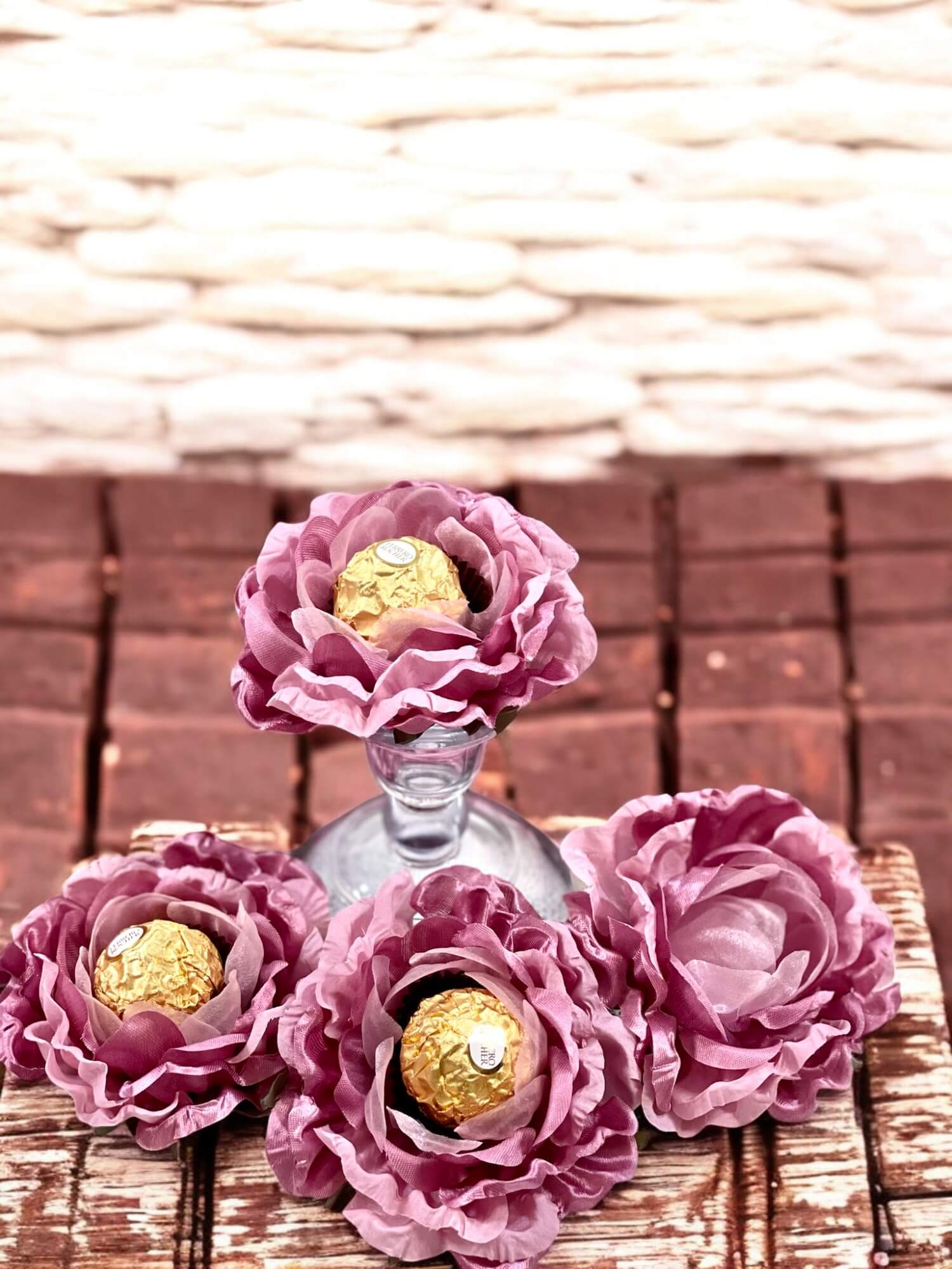 Dusty rose flowers centerpiece holding chocolate wrapped in gold foil  on a textured surface