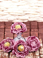 Dusty rose flowers centerpiece holding chocolate wrapped in gold foil  on a textured surface