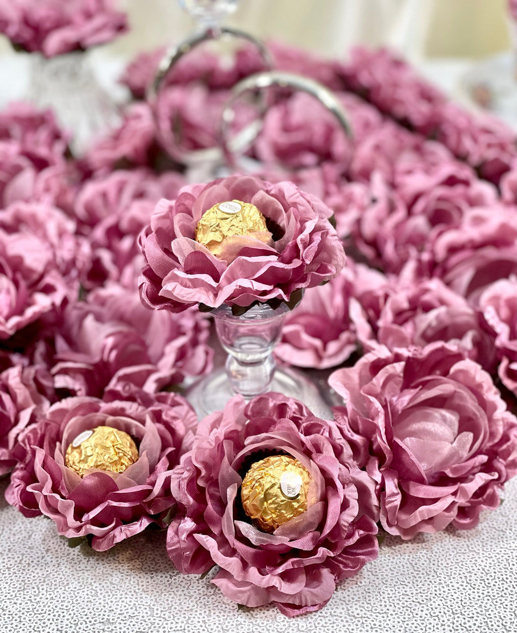 Dusty rose flowers centerpiece holding chocolate wrapped in gold foil  on a textured surface