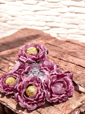 Dusty rose flowers centerpiece holding chocolate wrapped in gold foil  on a textured surface