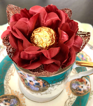 A decorative maroon and copper satin flower with a gold-colored chocolate bar held within.