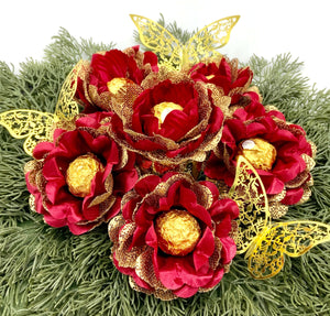 Decorative centerpiece with red and gold flowers holding a gold chocolate and butterfly accents,
