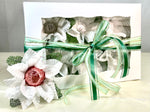 Image of a white box with green ribbon. The box comes with 6 flowers. These flowers are white with green accents. Each flower has a little cup in the middle which is used to hold sweets. Theses flowers are sweet holder. There is 1 flower sitting in front of the box. In the flower there is a chocolate truffle wrapped in rose gold foil.