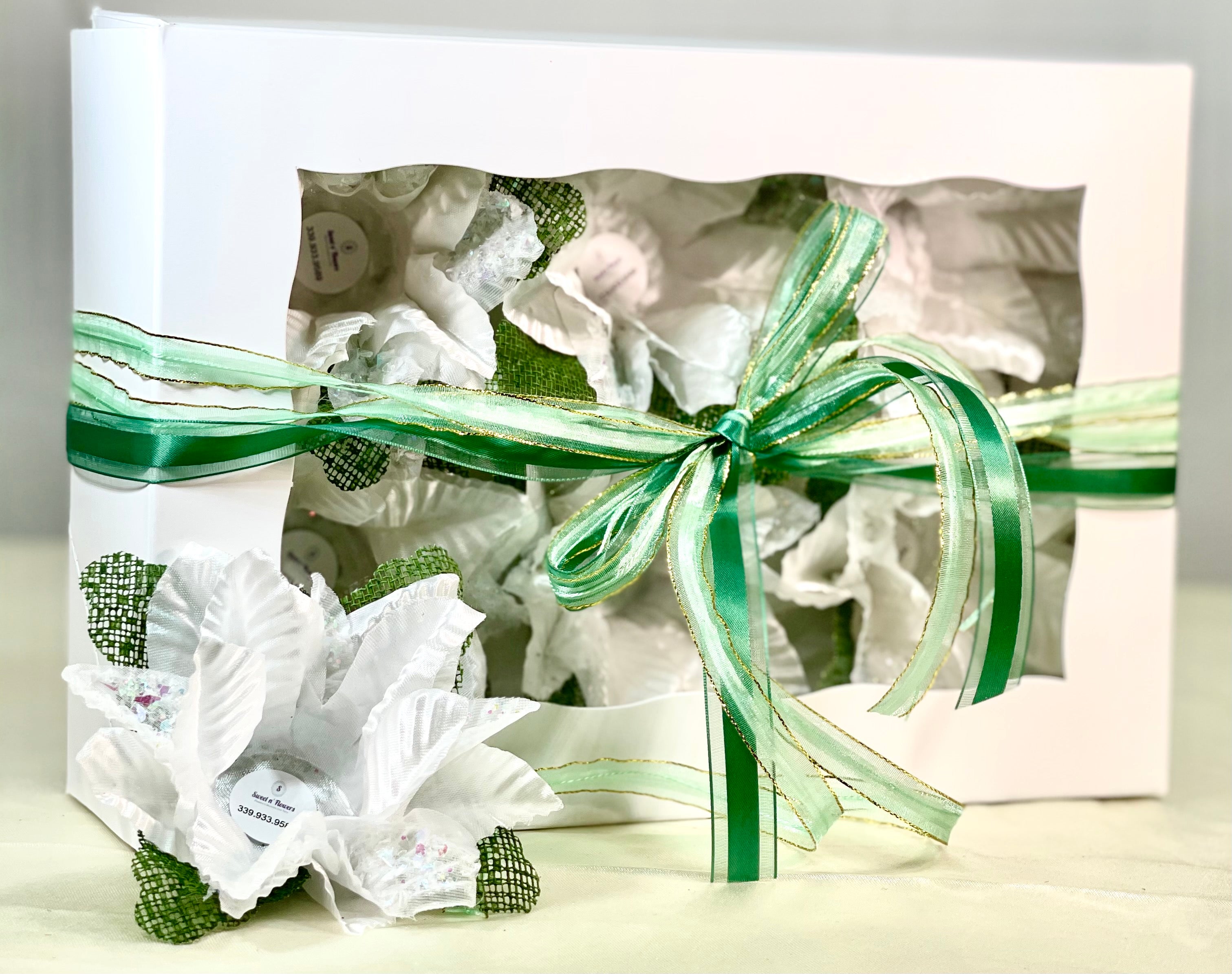 Image of a white box with green ribbon. The box comes with 6 flowers. These flowers are white with green accents. Each flower has a little cup in the middle which is used to hold sweets. Theses flowers are sweet holders.