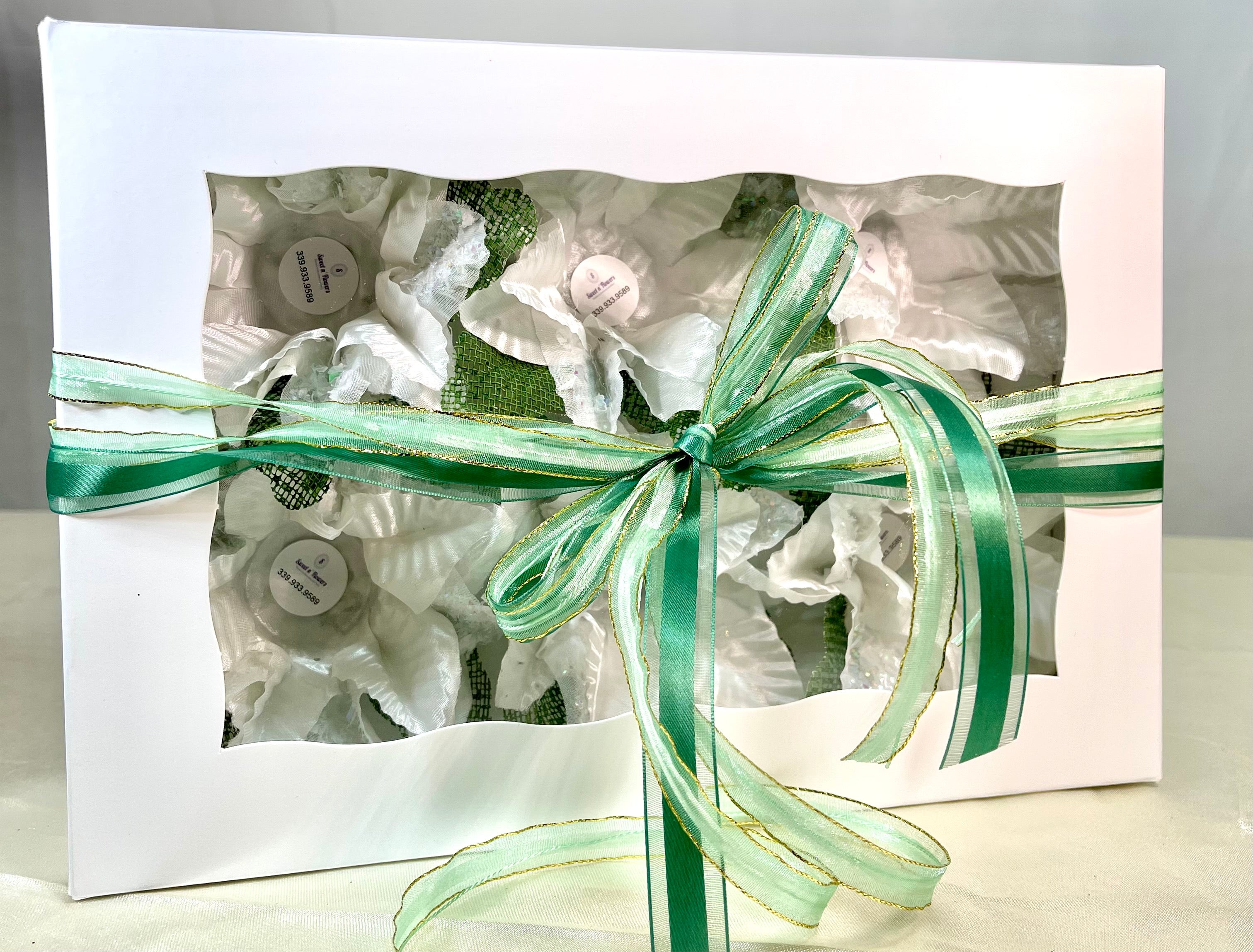 Image of a white box with green ribbon. The box comes with 6 flowers. These flowers are white with green accents. Each flower has a little cup in the middle which is used to hold sweets. Theses flowers are sweet holder.
